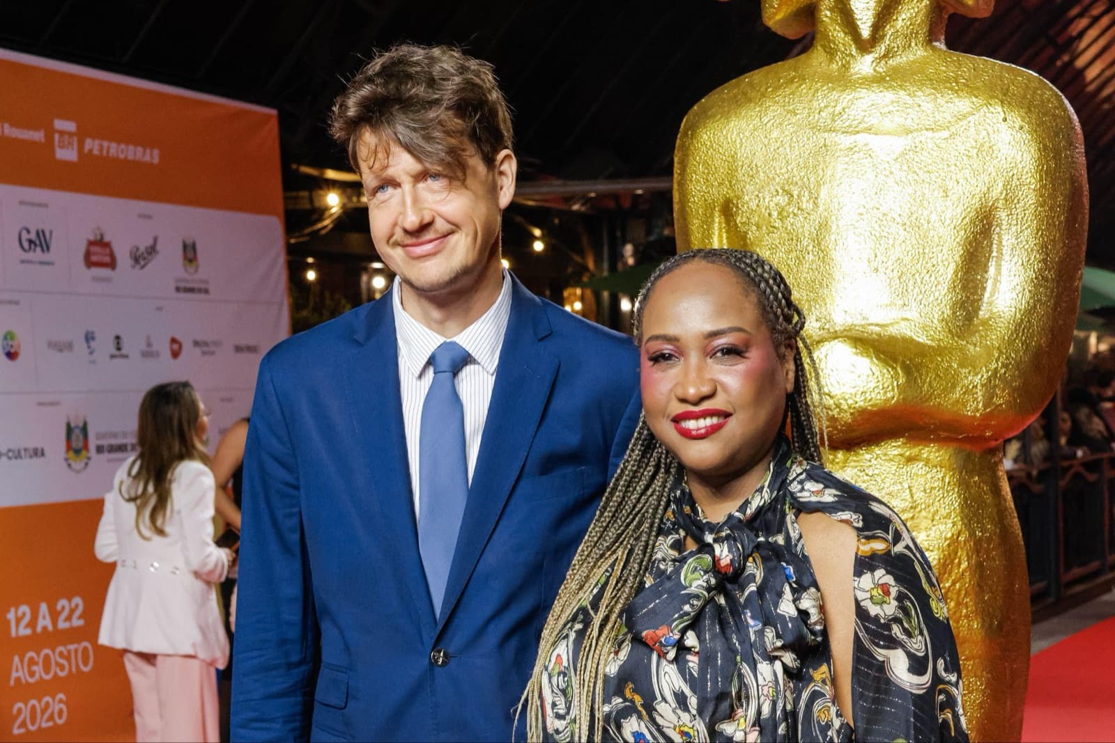 Sabrina Fidalgo e Yvan Rodic, diretores de “O Projeto”, no tapete vermelho ao lado da estátua do Kikito